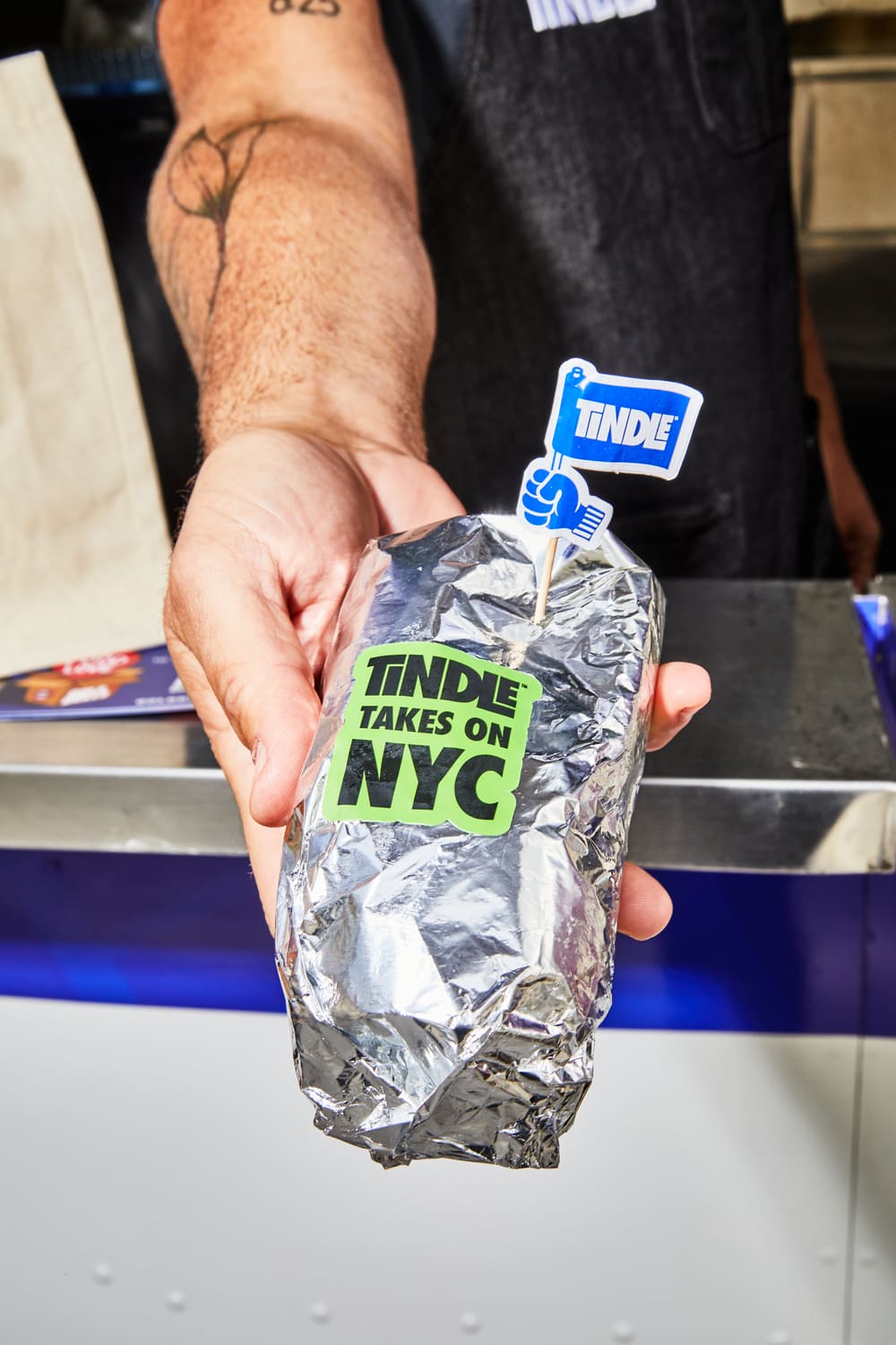 A person holding a foil-wrapped item with a "tindle takes on nyc" sticker.