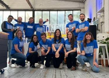 Group of individuals wearing matching blue t-shirts posing for a photo in a room with industrial decor.