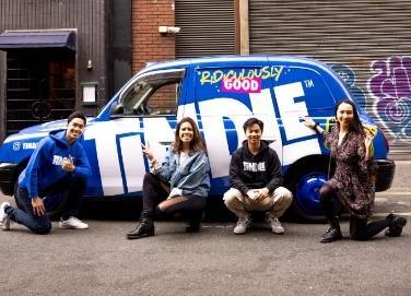Four people posing with a branded vehicle in an urban setting.