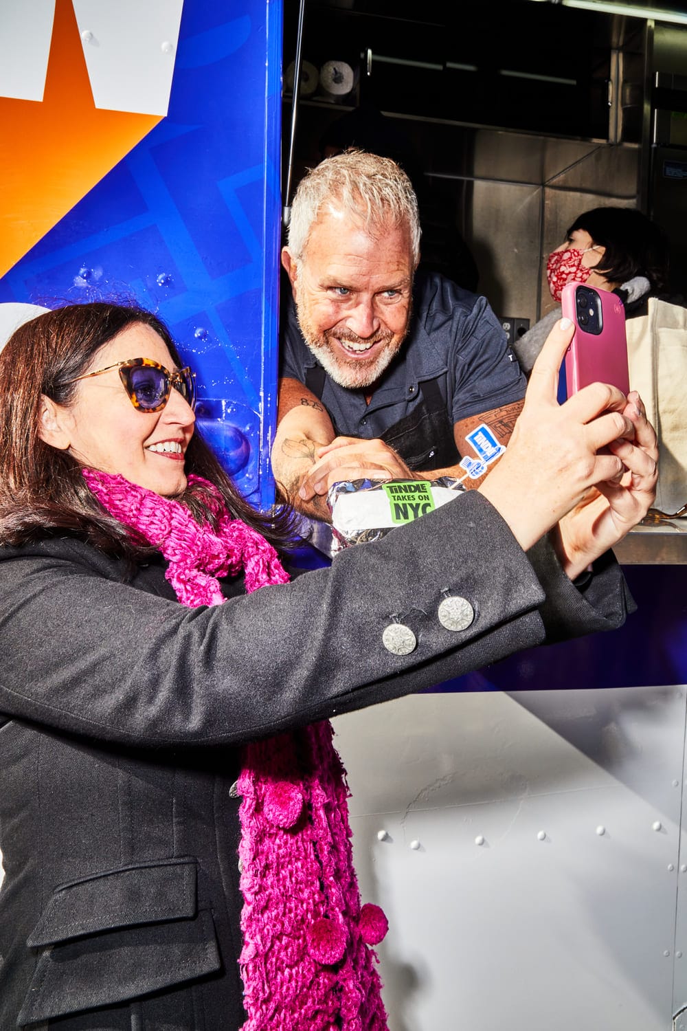 A person takes a selfie with a smiling chef at a food service window.
